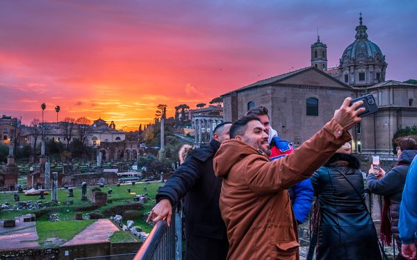 Three friends taking a selfie in front of a sunset at the Fora Romana in Roma, Italia.